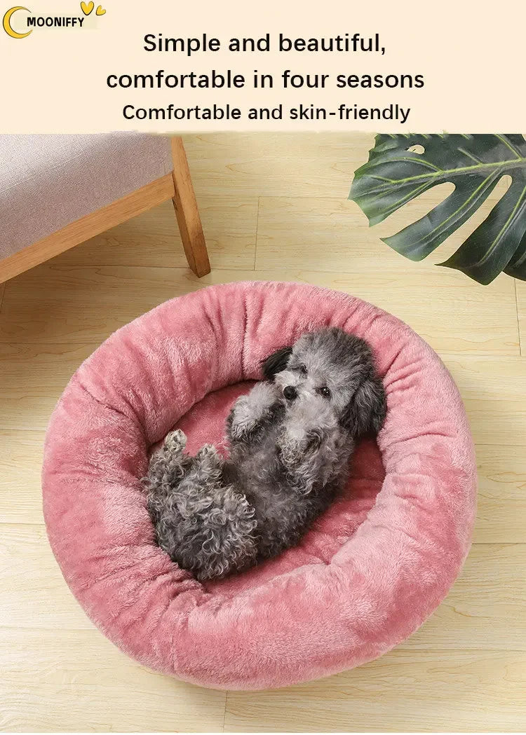 Small gray dog lying in a round pink plush pet bed on a wooden floor