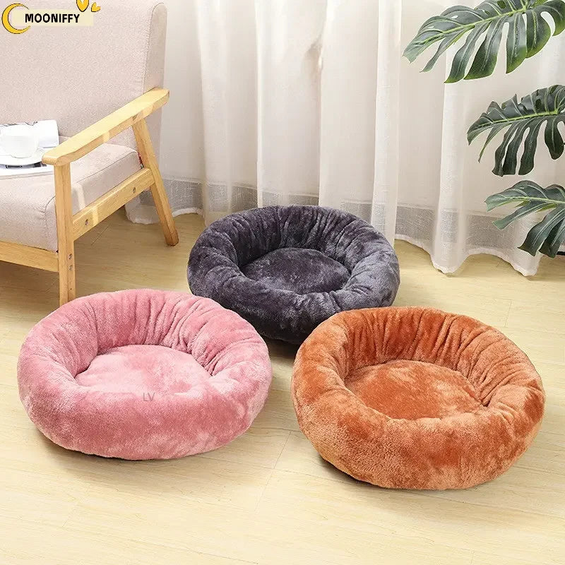 Three round plush pet beds in pink, gray, and brown on a light wood floor in a cozy living room.